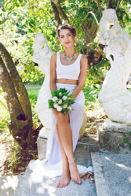 Photo gratuite mode portrait de la belle mariée créative, tenant un bouquet de lotus exotique, portant une tenue de mariage inhabituelle élégante et un gros collier de diamants.