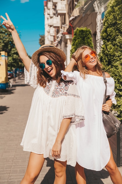 Mode portrait de deux jeunes femmes hippies élégantes brune et blonde modèles en journée ensoleillée d'été en vêtements hipster blanc posant