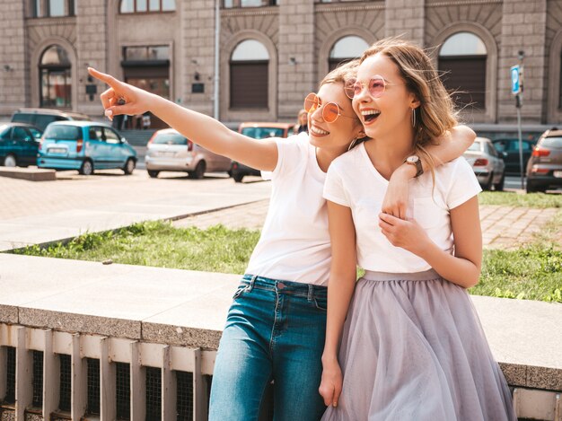 Mode portrait de deux jeunes femmes hippies élégantes brune et blonde modèles en journée ensoleillée d'été en vêtements hipster blanc posant