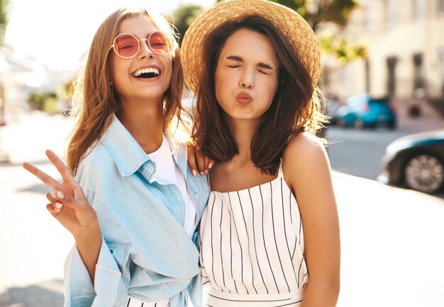 Mode portrait de deux jeunes mannequins hippies élégantes brune et blonde en journée ensoleillée d'été dans des vêtements hipster posant sur le fond de la rue. Sans maquillage