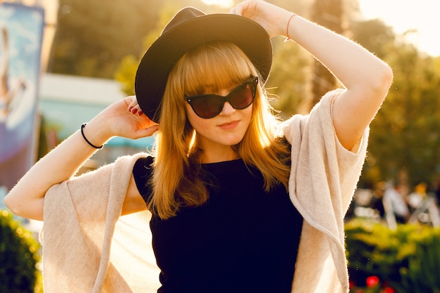 mode portrait de jeune femme brune à lunettes de soleil noires contre le soleil couchant, avec sac en cuir.