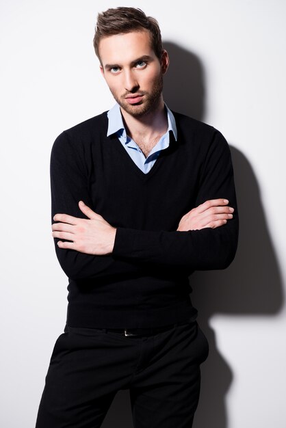 Mode portrait de jeune homme en pull noir et chemise bleue avec les bras croisés.