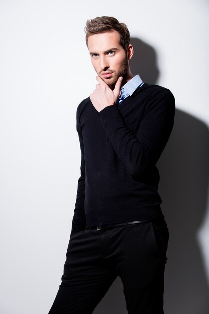 Mode portrait de jeune homme en pull noir et chemise bleue avec des ombres contrastées.