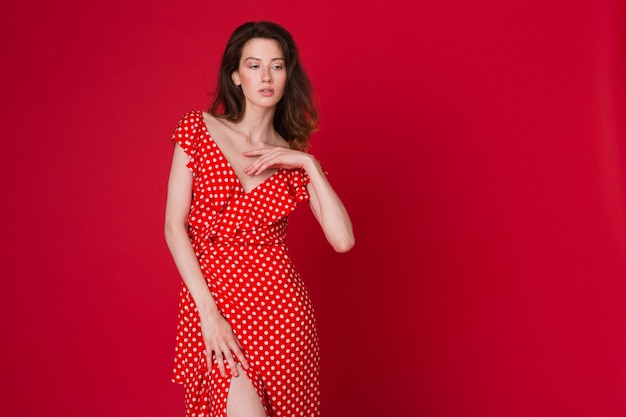 Mode portrait de jolie jeune femme souriante en robe à pois rouge sur studio rouge