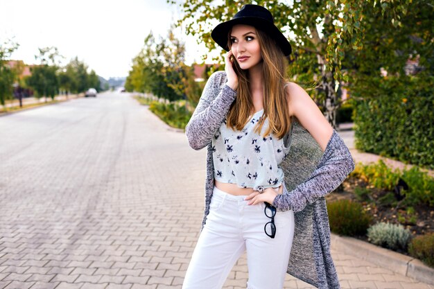 Mode portrait en plein air de jeune femme blonde assez sensuelle posant à la campagne au moment de l'automne, portant un élégant hipster décontracté et un chapeau, des couleurs vintage douces, marchant seul.