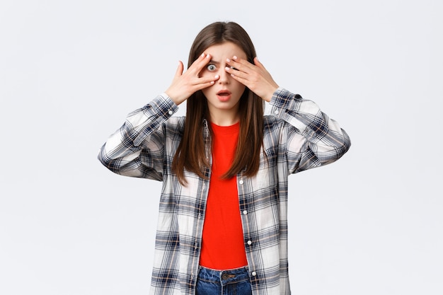 Mode de vie, différentes émotions, concept d'activités de loisirs. Jeune jolie femme choquée et sans voix en chemise à carreaux, couvre les yeux d'une chose effrayante mais jette un coup d'œil à travers les doigts