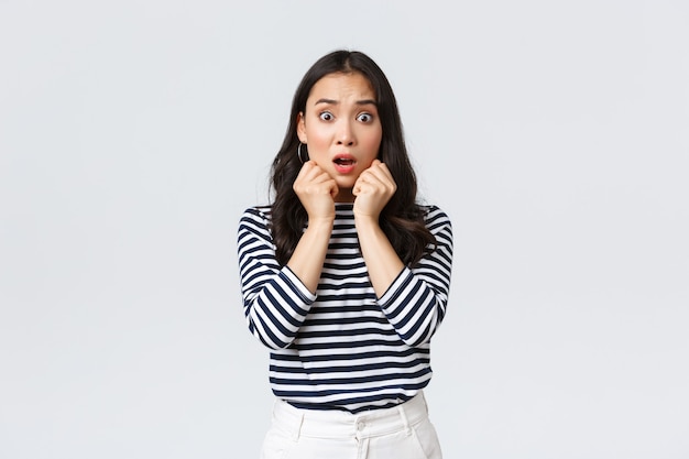 Mode de vie, émotions des gens et concept décontracté. Une fille asiatique effrayée et inquiète en chemise rayée, haletant d'un air alarmé, a eu des ennuis, découvre la vérité choquante, debout sur fond blanc