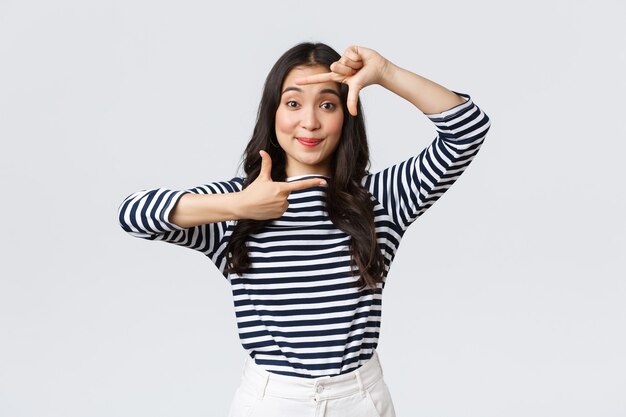 Mode de vie, émotions des gens et concept décontracté. Jolie fille asiatique créative imaginant, capturez le moment avec un geste de cadres à main, souriant amusé, restant positif et heureux, fond blanc