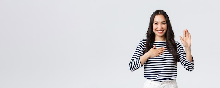 Photo gratuit mode de vie émotions des gens et concept décontracté jolie fille coréenne honnête et sincère faisant la promesse de lever le bras et de tenir la main sur le cœur en souriant tout en jurant dire la vérité prêter serment