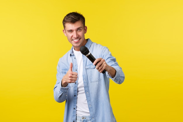 Mode de vie, émotions des gens et concept de loisirs d'été. Bel homme blond charismatique, chantant une chanson avec microphone, souriant effronté et montrant le pouce vers le haut, profitant d'un karaoké.