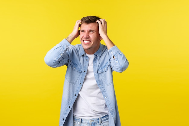 Mode de vie, émotions des gens et concept de loisirs d'été. Un homme blond inquiet et anxieux attrape la tête et a l'air désespéré, joue, regarde l'échec, perd et est en détresse, regarde à gauche.