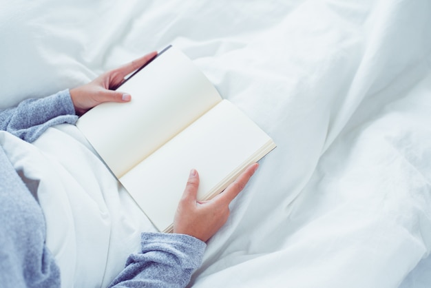 Mode de vie heureux jeune femme asiatique profitant de s&#39;allonger sur le lit en lisant un livre plaisir en vêtements de loisirs