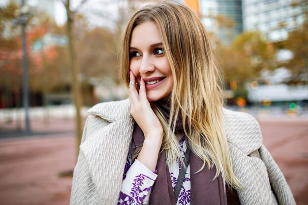 Mode de vie en plein air portrait positif de jolie femme blonde souriante fin profiter du temps, tenue élégante glamour, robe et manteau, couleurs chaudes, printemps automne.