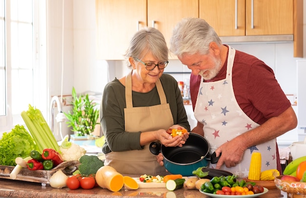 Mode de vie végétarien. beau couple de personnes âgées aux cheveux blancs dans la cuisine prépare une soupe de légumes. la femme met des légumes hachés dans la marmite, sur la table un mélange de légumes crus de saison