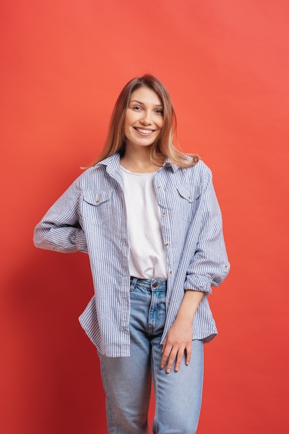 Modèle assez féminin posant avec une expression de visage souriant sur mur rouge