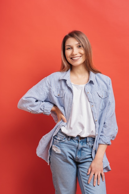 Modèle assez féminin posant avec une expression de visage souriant sur mur rouge