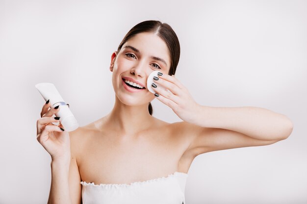 Modèle aux yeux verts avec sur un mur blanc. La brune hydrate le visage avec la crème Dove.