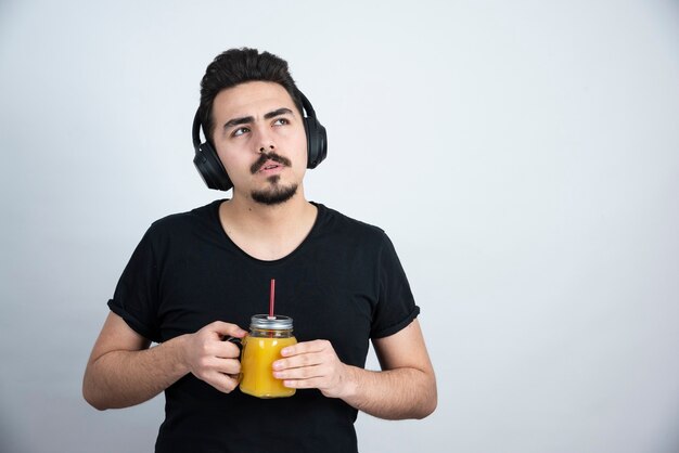 modèle de beau mec dans les écouteurs tenant une tasse en verre avec du jus d'orange.