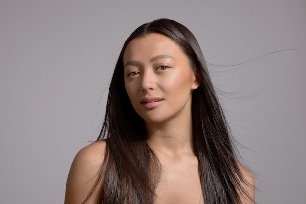 Modèle de beauté brune modèle de race mixte avec de longs cheveux raides soufflant le maquillage naturel de la peau idéale