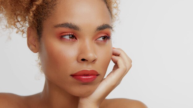 Modèle blonde noire métisse aux cheveux bouclés et au maquillage rouge qui lui touche la joue