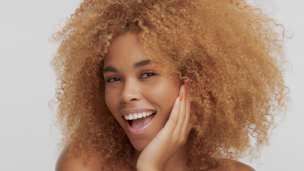 Modèle blonde noire métisse aux cheveux bouclés et riant et mettant son visage à portée de main