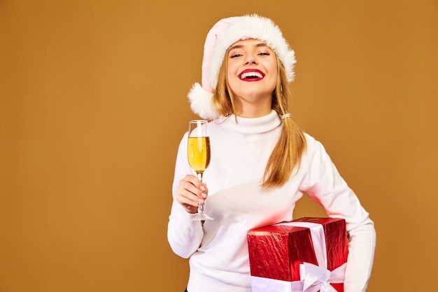 Modèle avec bonnet de Noel et grand coffret cadeau buvant du champagne sur mur d'or