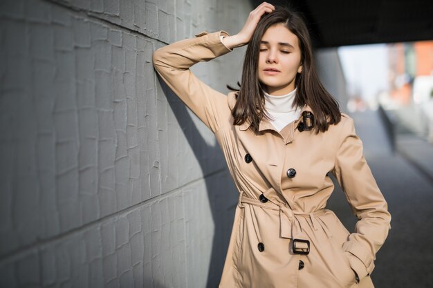 Modèle brune aux yeux vêtus reste près du mur gris à l'extérieur