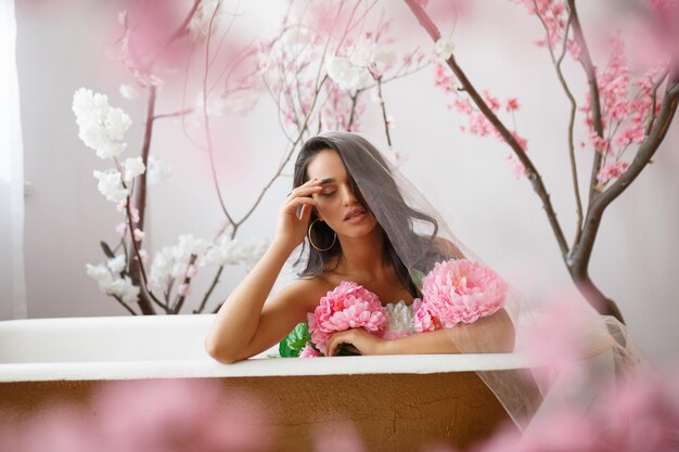 Modèle chaud assis dans une baignoire avec bouquet de fleurs Photo de haute qualité