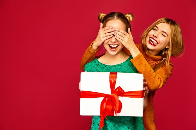 Modèle couvrant les yeux de son amie et lui donnant un grand coffret cadeau