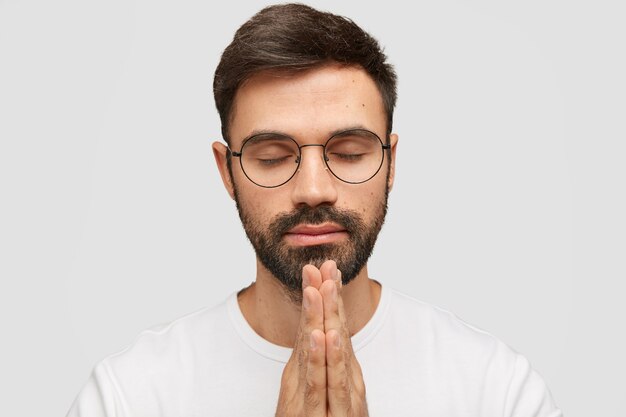 Le modèle du jeune homme barbu concentré garde les paumes dans le geste de prière, croit en la bonne fortune.