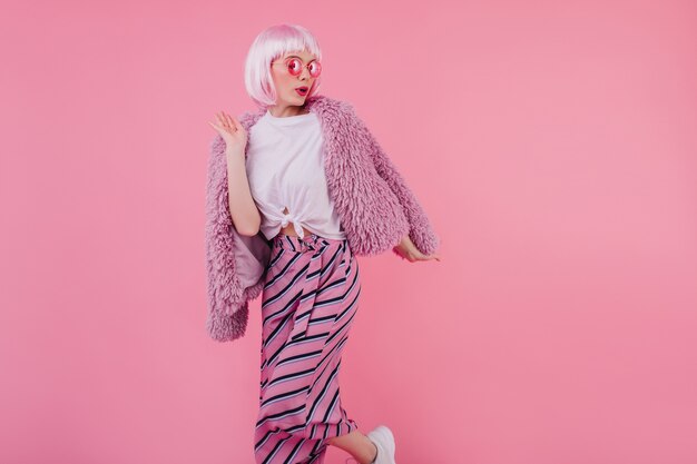 Modèle féminin adorable dans des vêtements à la mode posant avec une expression de visage sérieuse. Photo intérieure d'une fille caucasienne glamour au Pérou isolé sur un mur rose