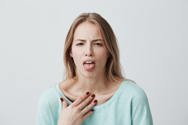 Le modèle féminin blond insatisfait fronce les sourcils, a une expression dégoûtante, montre la langue, exprime le non-respect, irrité par quelqu'un, rejette de faire quelque chose. Personnes et expressions faciales négatives