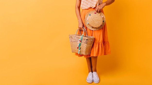 Modèle féminin bronzé posant en studio avec chapeau de paille Dame caucasienne bien habillée en jupe orange tenant un sac d'été