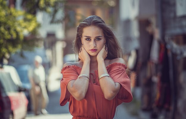 Modèle féminin dans une robe rouge-orange dans une rue avec une surface floue