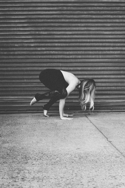 Modèle féminin en forme attrayant pratiquant le yoga près d'un garage sur le trottoir tourné en niveaux de gris
