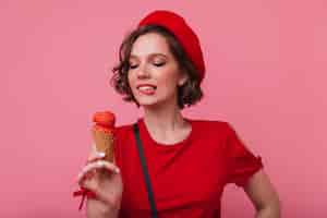 Photo gratuite modèle féminin inspiré avec une coiffure ondulée regardant la crème glacée avec le sourire. fille française sensuelle en béret appréciant le dessert.