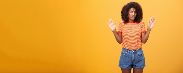 Photo gratuite modèle féminin à la peau foncée, peu sûr et triste, en t-shirt et short rayés à la mode, levant les bras dans