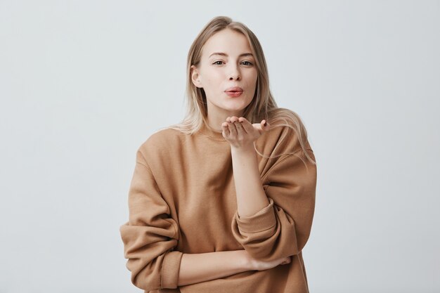 Modèle féminin rêveur attrayant avec des cheveux blonds fait la moue, envoie des baisers