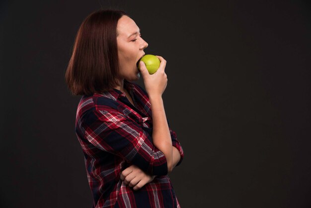 Modèle féminin en tenues de collection automne hiver tenant une pomme verte et en prenant une bouchée.