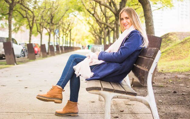 Modèle féminin vêtu chaud, assis au banc de parc automne