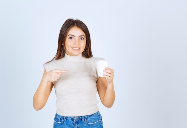 Un modèle de femme souriante pointant vers un gobelet en plastique et posant.