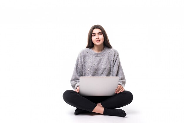 Modèle fille brune en pull gris s'asseoir sur le sol et travailler studie sur son ordinateur portable