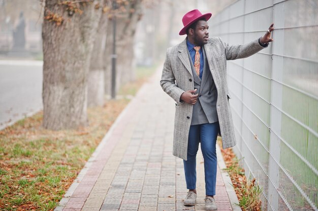 Modèle d'homme afro-américain élégant en manteau gris veste cravate et chapeau rouge