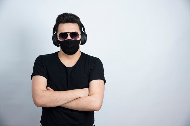 Modèle homme brune avec des lunettes de soleil posant dans un masque médical et des écouteurs.