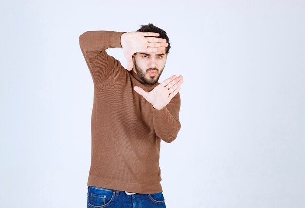 Photo gratuite modèle de jeune bel homme regardant à travers un cadre formé par ses mains.