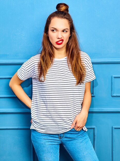 Modèle jeune femme élégante dans des vêtements d'été décontractés avec des lèvres rouges, posant près du mur bleu