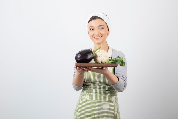 Un modèle de jeune femme mignonne tenant une assiette en bois avec des aubergines et du chou-fleur