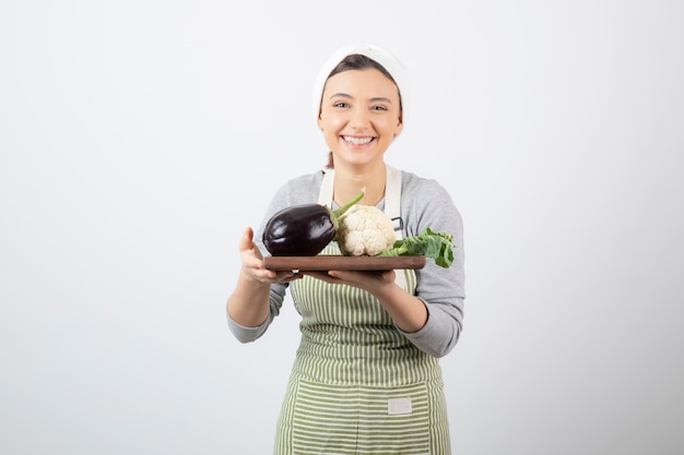 Un modèle de jeune femme mignonne tenant une assiette en bois avec des aubergines et du chou-fleur