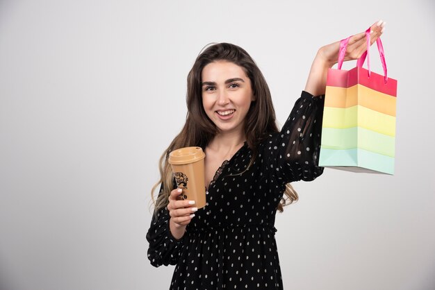 Modèle de jeune femme montrant un sac de magasin et tenant une tasse de café