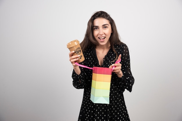 Modèle de jeune femme ouvrant un sac de magasin et tenant une tasse de café